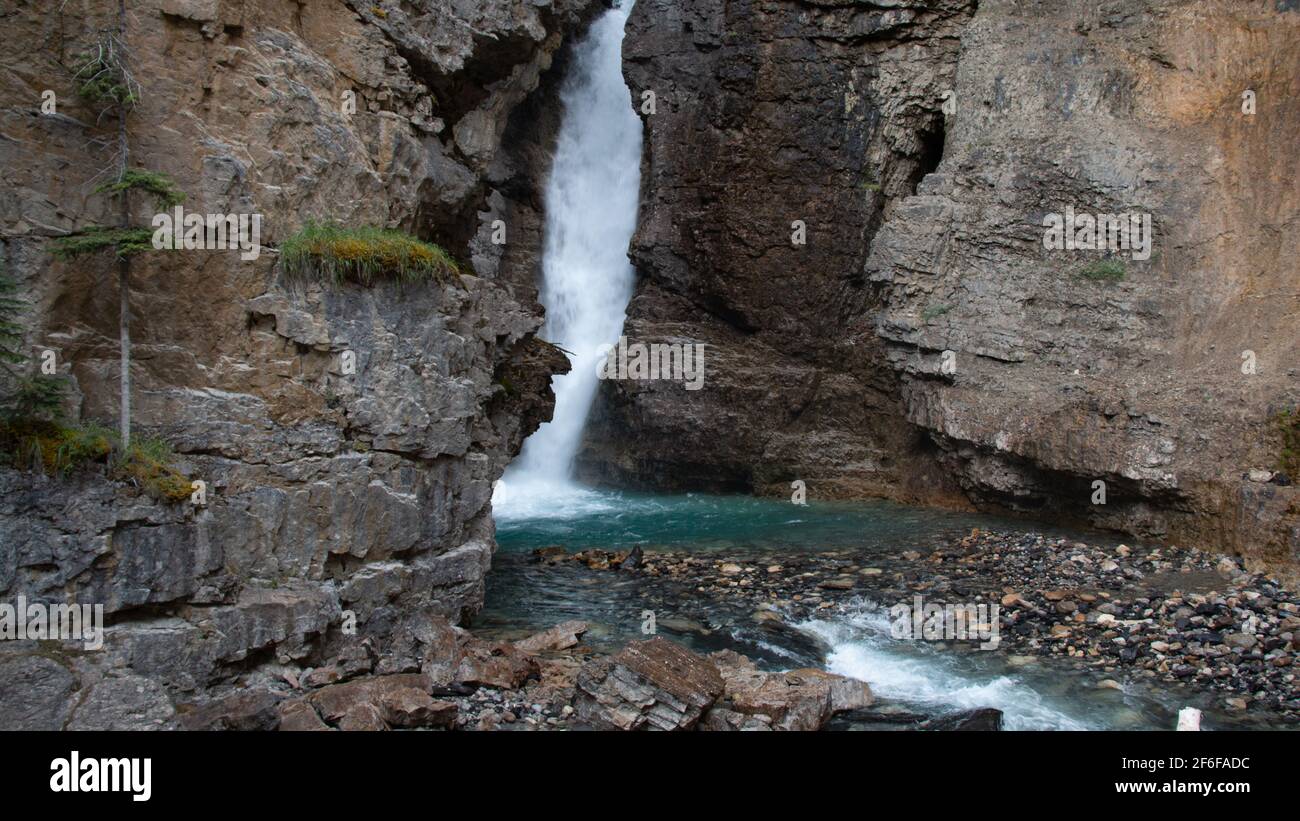 Le Upper Falls presso il Johnston Canyon di Banff, Alberta, Canada, si affacciano da dietro una grande parete rocciosa. Foto Stock