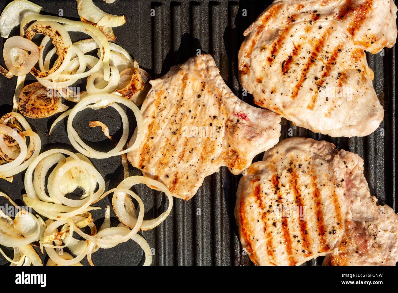 Vista dall'alto di costolette di maiale e cipolle che sfrigolano su portatile mini grill elettrico cucina casalinga all'aperto Foto Stock