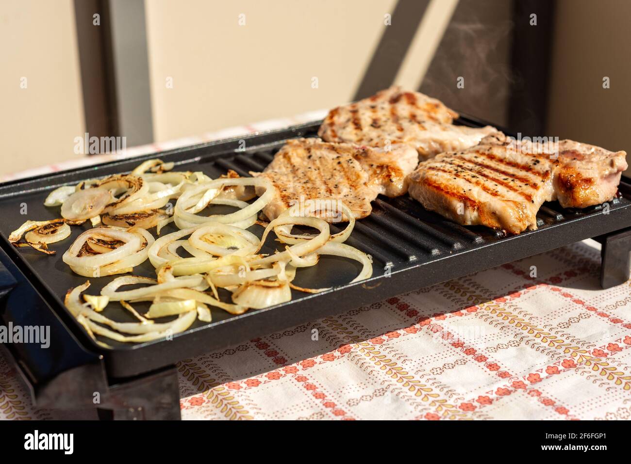 Carne e cipolle sfrigolanti su mini grill elettrico portatile cottura all'aperto Foto Stock