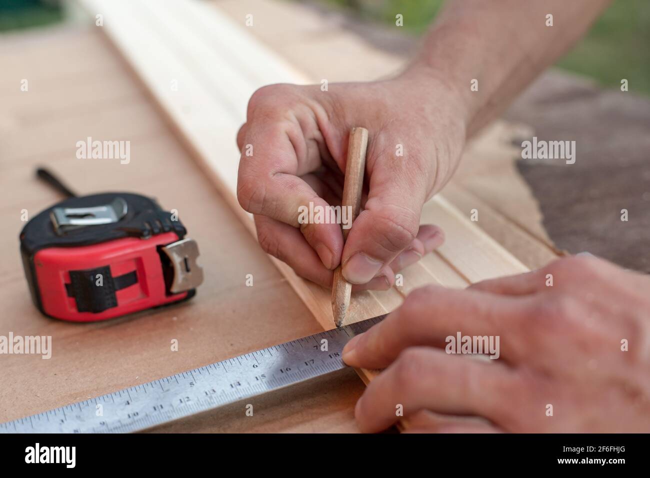 Le mani del falegname prendono le misure con un righello metallico su una tavola di legno e contrassegnano la lunghezza richiesta con una matita. Foto Stock