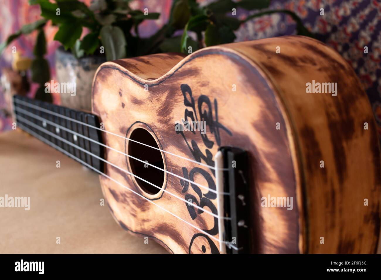 Closeup di un ukulele carteggiato e dipinto in Ontario, Canada con un cactus di Natale seduto dietro di esso contro un arazzo mandala, 2021. Foto Stock