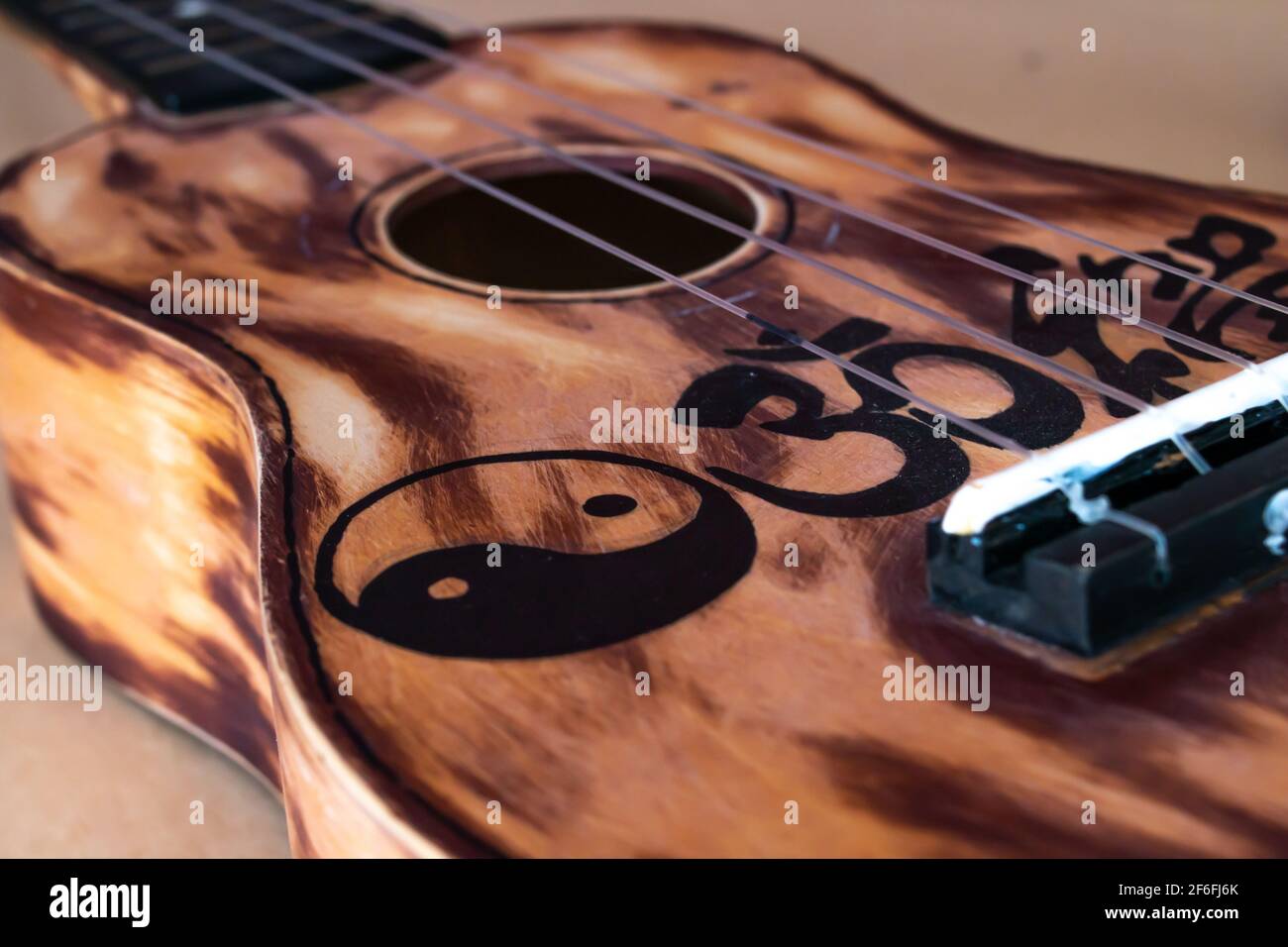 Closeup di un ukulele carteggiato e dipinto in Ontario, Canada con un cactus di Natale seduto dietro di esso contro un arazzo mandala, 2021. Foto Stock