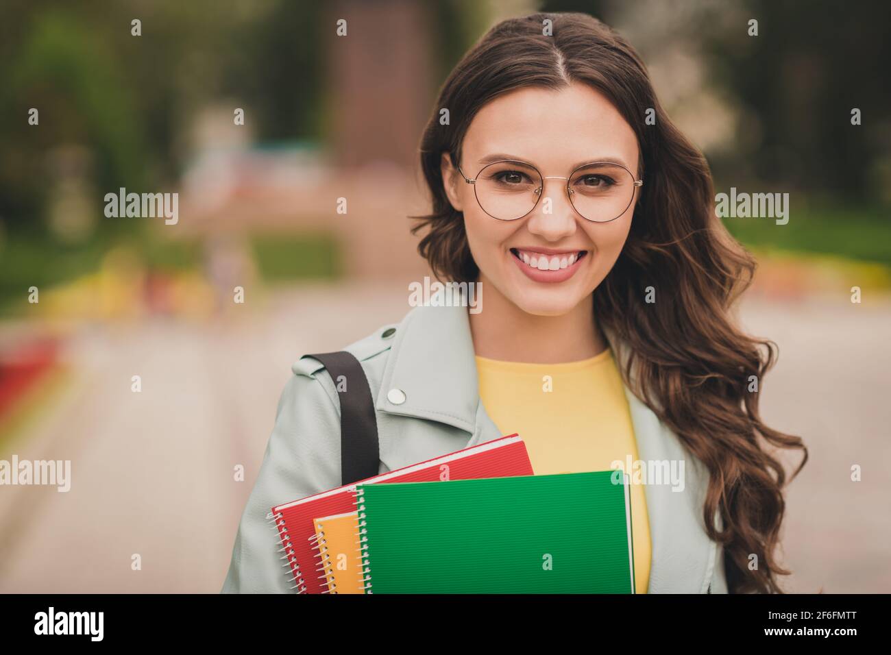 Foto di splendido acconciatura sventolosa soddisfatta giovane ragazza che sorride guarda la macchina fotografica tornare a casa dopo le lezioni all'aperto Foto Stock