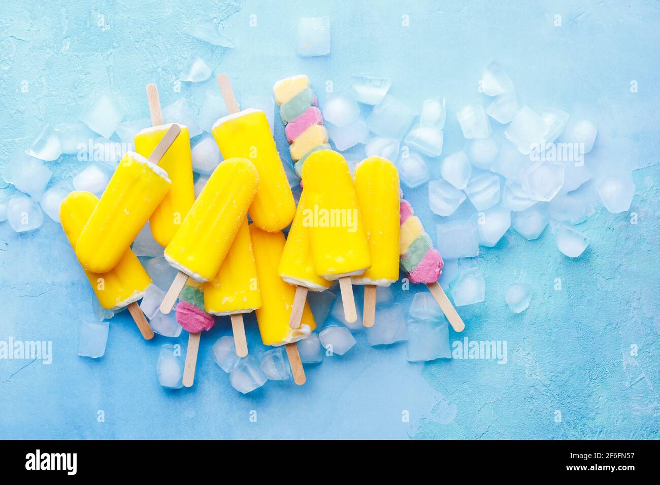 Il gelato alla frutta esotica si attacca su sfondo blu con cubetti di ghiaccio. Vista dall'alto, spazio vuoto Foto Stock