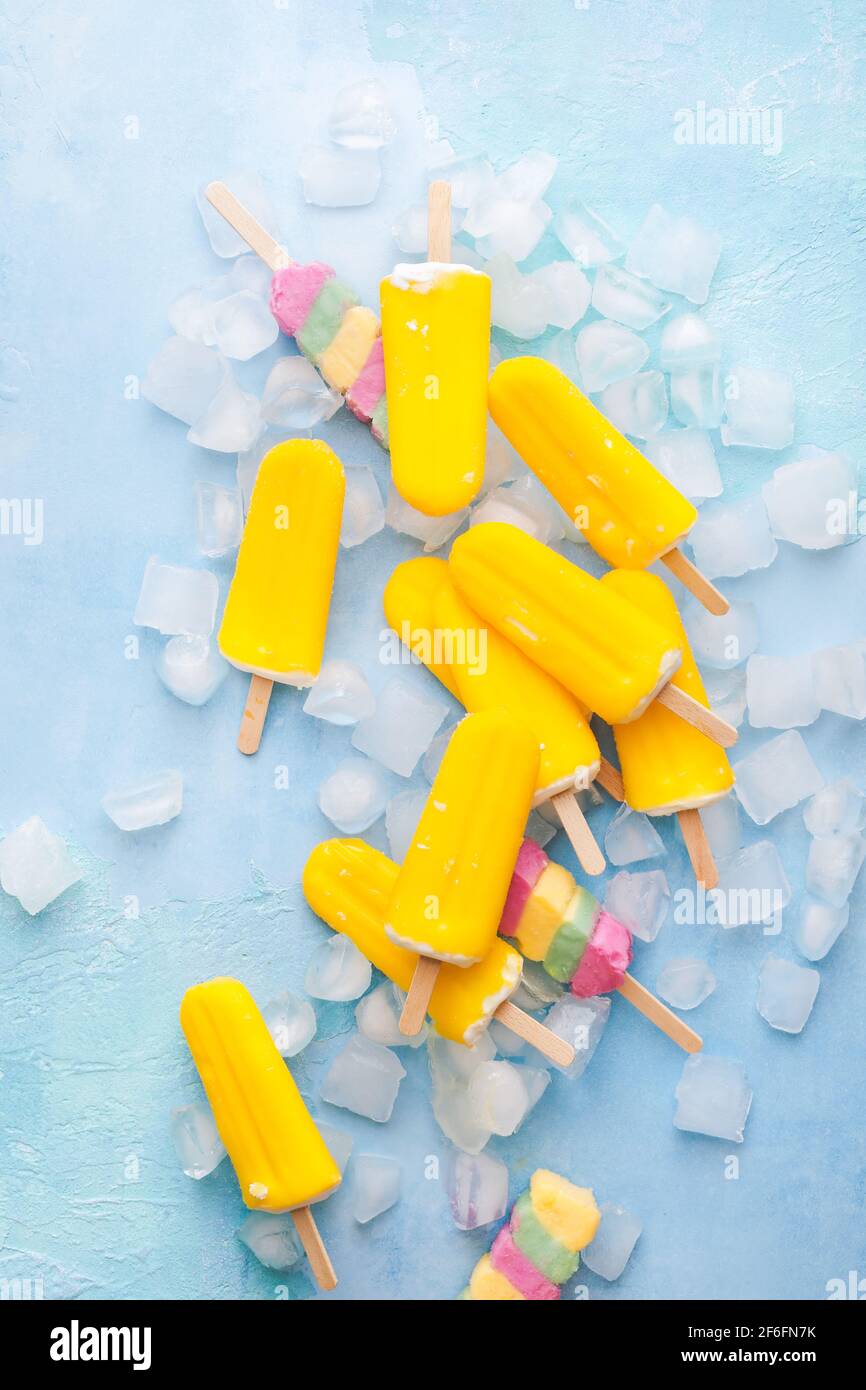 Il gelato alla frutta esotica si attacca su sfondo blu con cubetti di ghiaccio. Vista dall'alto, spazio vuoto Foto Stock