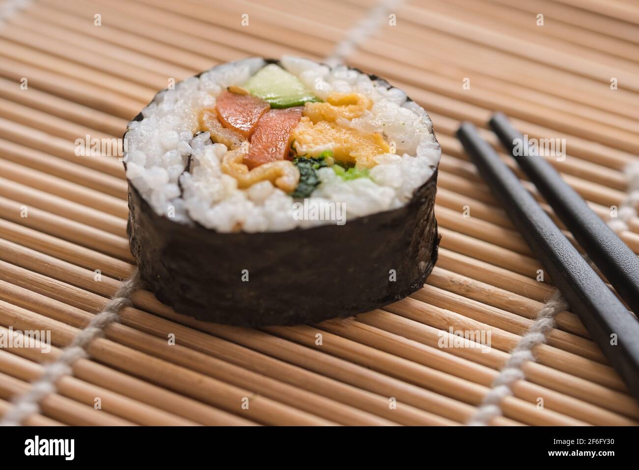 Gimbap coreano su un tappeto a rulli suhi accanto alle bacchette Foto Stock