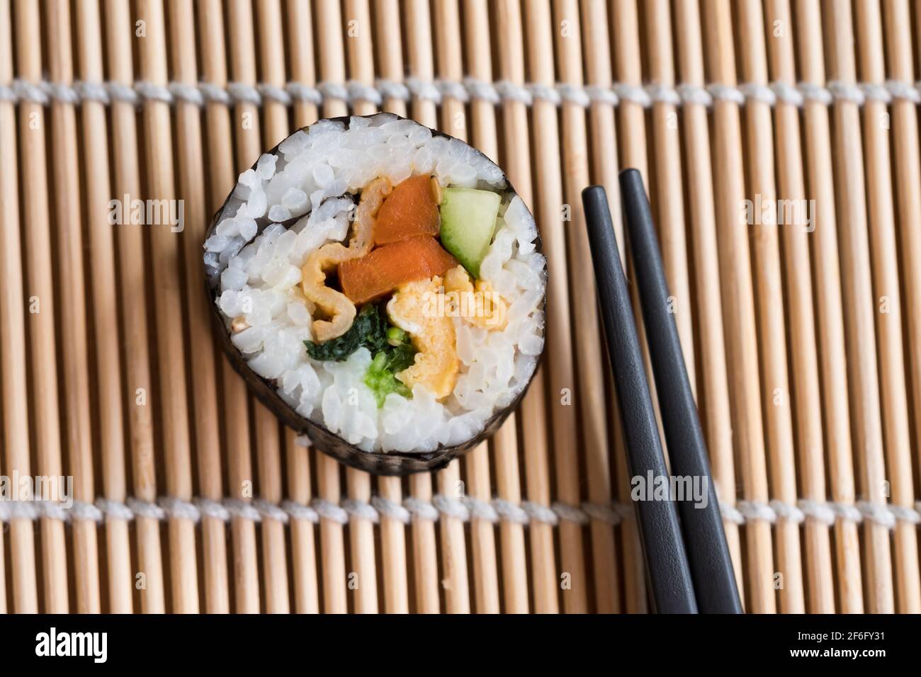 Gimbap coreano su un tappeto a rulli suhi accanto alle bacchette Foto Stock
