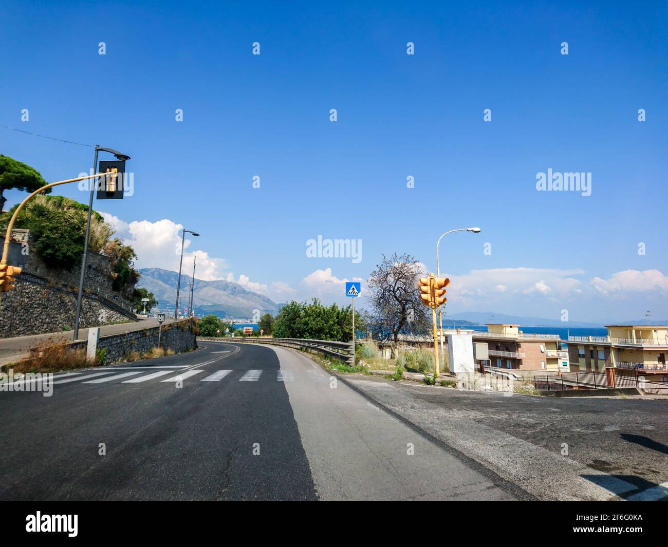 Guida su strada vuota della costa italiana con incrocio, semafori gialli e cielo blu chiaro. Vista panoramica sulla regione mediterranea Foto Stock