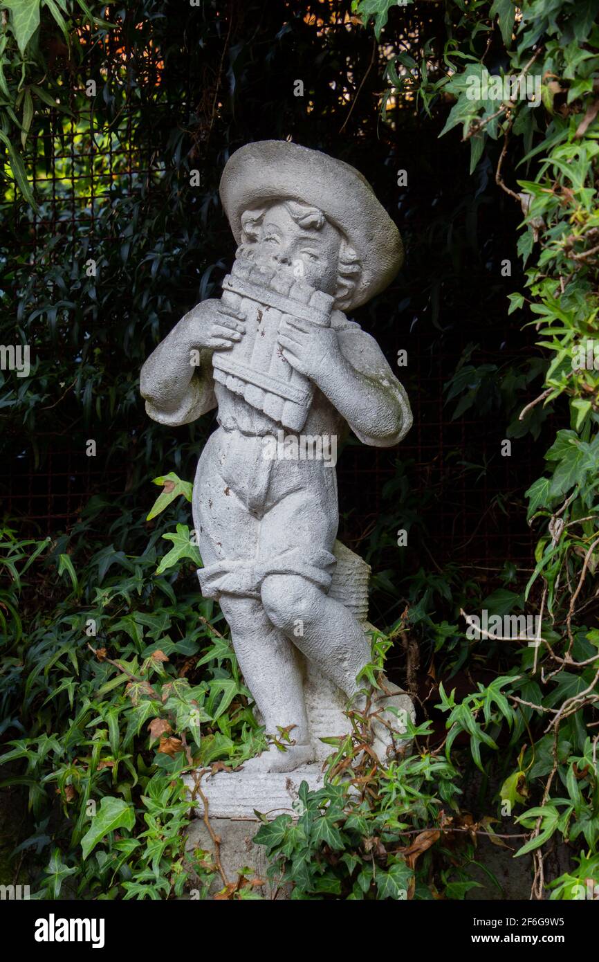 Vecchia statua bianca intemperie di un ragazzo che gioca una padella flauto circondato da edera Foto Stock