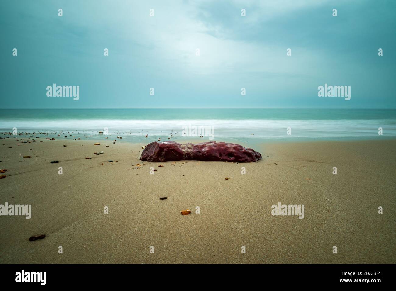 Roccia rossa su una spiaggia con mare liscio in serena lunga esposizione. Seascape minimalista. Foto Stock