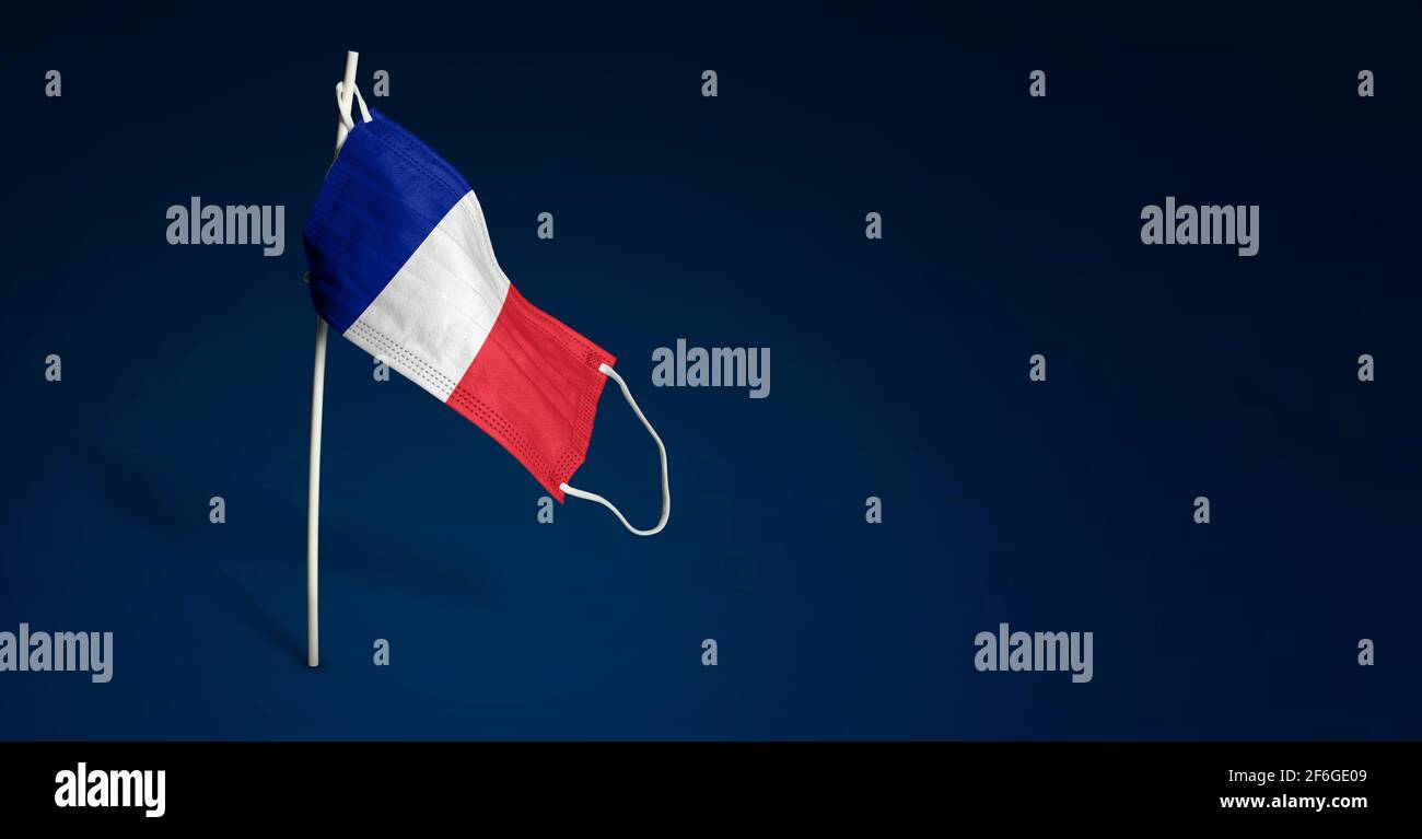 Maschera francese su sfondo blu scuro. Bandiera ondulata della Francia dipinta su maschera medica sul palo. Flag di attacco del virus. Concetto della bandiera della lotta agai Foto Stock
