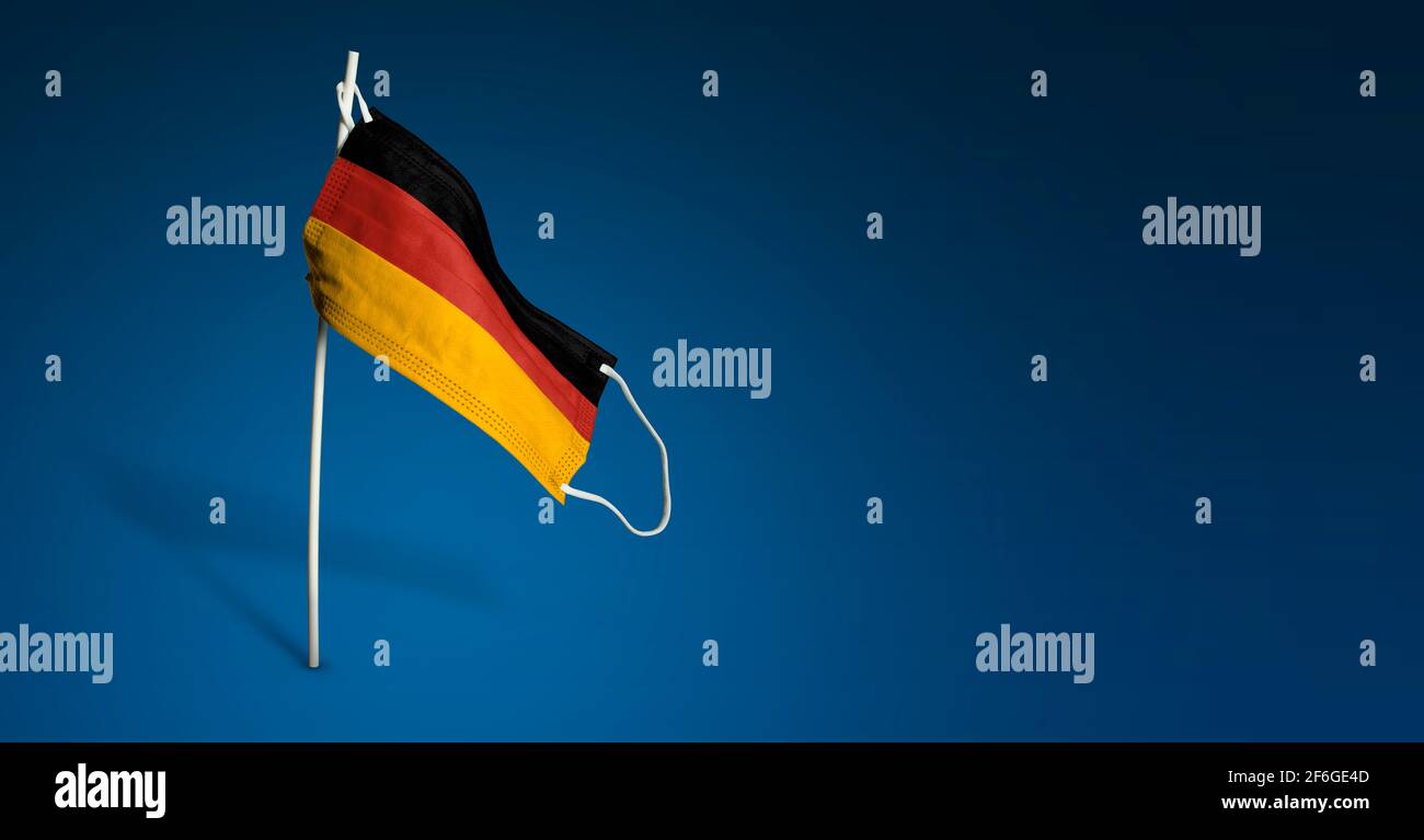 Maschera Germania su sfondo blu scuro. Bandiera ondulata della Germania dipinta su maschera medica sul palo. Flag di attacco del virus. Concetto del banner della Fight ag Foto Stock