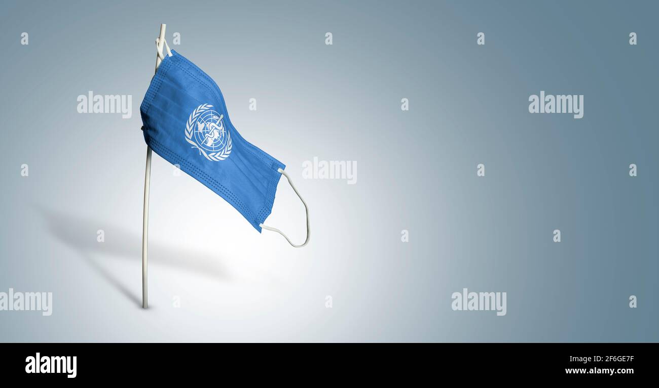 Maschera dell'Organizzazione Mondiale della Sanità su sfondo azzurro. Bandiera sventolante di CHI dipinse su maschera medica sul palo. Flag di attacco del virus. Concetto del banner Foto Stock