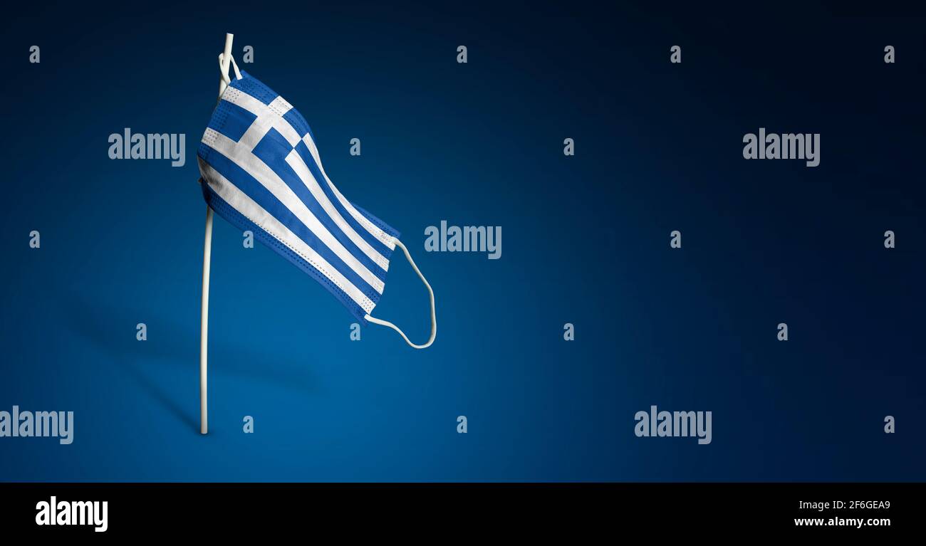 Maschera greca su sfondo blu scuro. Bandiera ondulata della Grecia dipinta su maschera medica sul palo. Flag di attacco del virus. Concetto della bandiera della lotta agai Foto Stock
