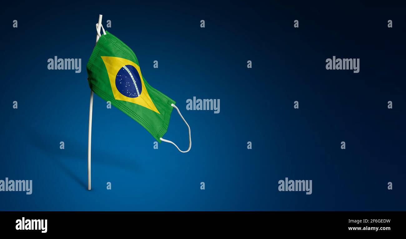 Maschera Brasile su sfondo blu scuro. Bandiera ondulata del Brasile dipinta su maschera medica sul palo. Flag di attacco del virus. Concetto della bandiera della lotta agai Foto Stock