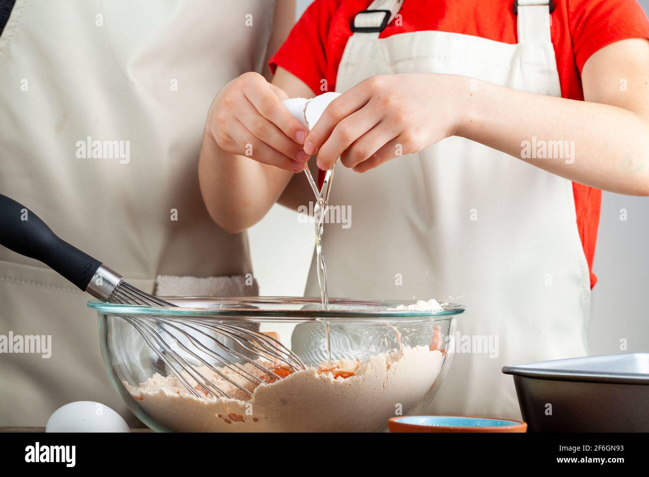 madre caucasica e piccola figlia che cucinano insieme il concetto con ragazza che cerca di rompere un uovo in una ciotola di la torta si mescola mentre preparano la registrazione Foto Stock