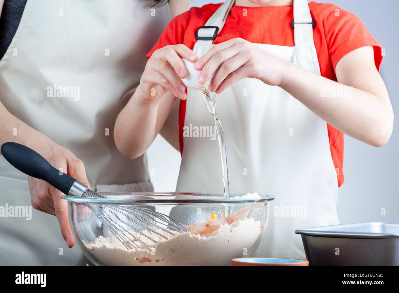 madre caucasica e piccola figlia che cucinano insieme il concetto con ragazza che cerca di rompere un uovo in una ciotola di la torta si mescola mentre preparano la registrazione Foto Stock