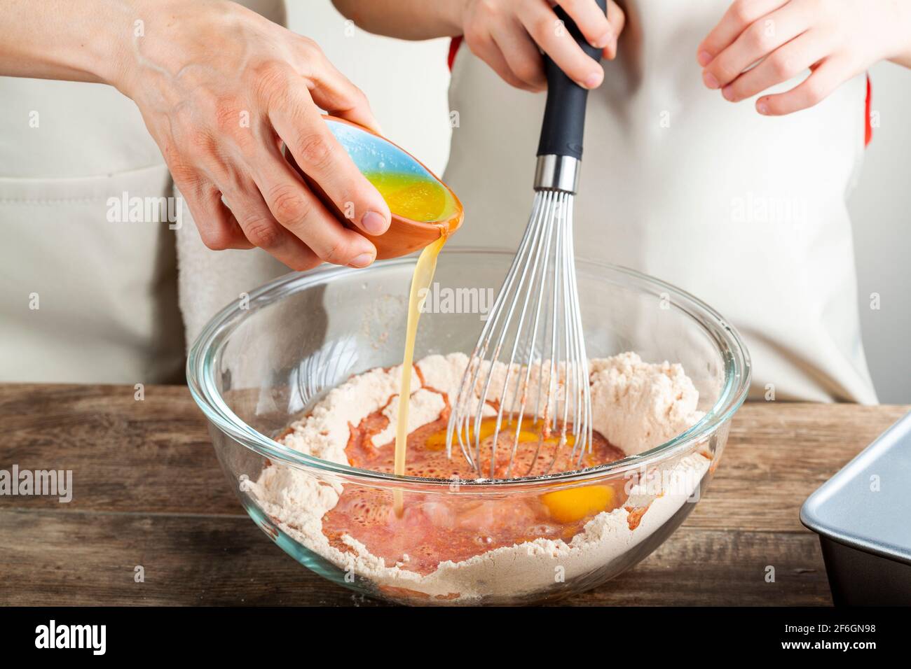 Madre e figlia che cucinano insieme nel concetto della cucina con la ragazza che tiene un whisk e la donna che versa con cura burro fuso o tuorlo d'uovo in Foto Stock