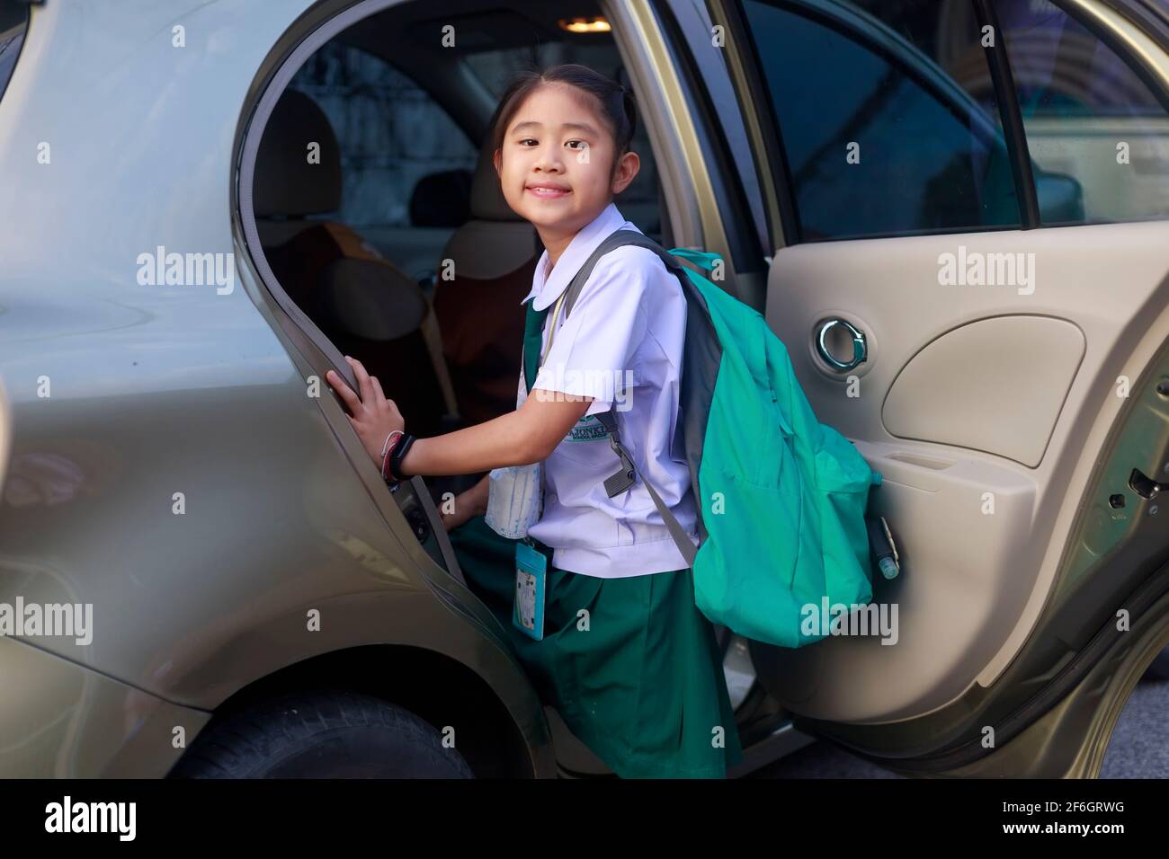 Asian School Girl indossa divisa scolastica e porta uno zaino verde salire sull'autobus per andare a scuola al mattino. Felice bambino della scuola primaria ottenere Foto Stock