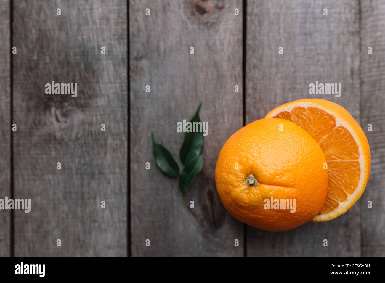 Metà di frutta arancione su sfondo grigio di legno. Polpa di arancia e foglie verdi Foto Stock