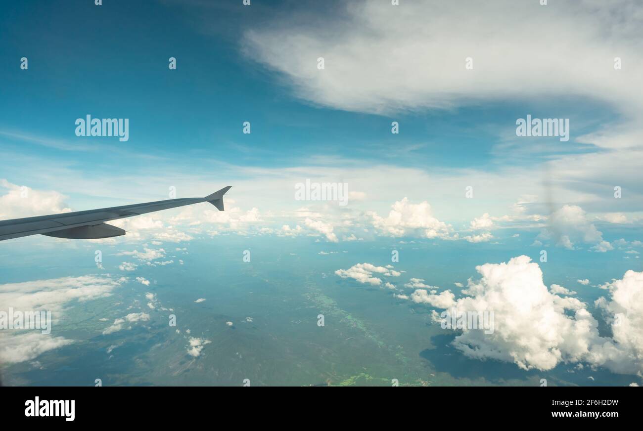 Vista dal piano interno attraverso la finestra piana su cielo blu, nuvole bianche e montagna verde. Volo aereo commerciale per viaggi estivi. Ala piana. Foto Stock