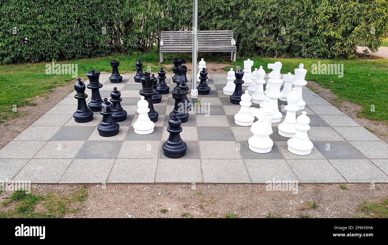 Gioco di scacchi nel parco esterno nel gigante verde campo area pavimento scacchi figure bianco nero ricreazione hobby torneo tempo libero strategia estate Foto Stock
