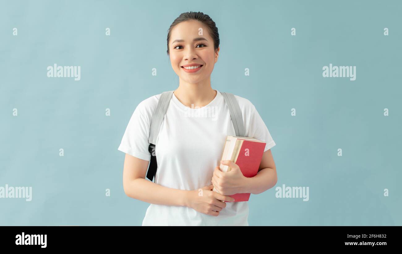 Donna studentesca che indossa uno zaino che tiene il notebook su sfondo blu isolato con un volto felice Foto Stock
