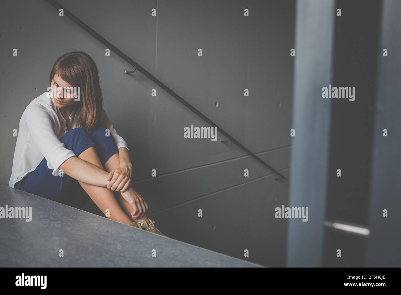 Giovane donna depressa seduta in una scala, perdita di lavoro a causa della pandemia del coronavirus, epidemia di Covid-19. Disoccupazione, crisi economica, difficoltà finanziarie Foto Stock