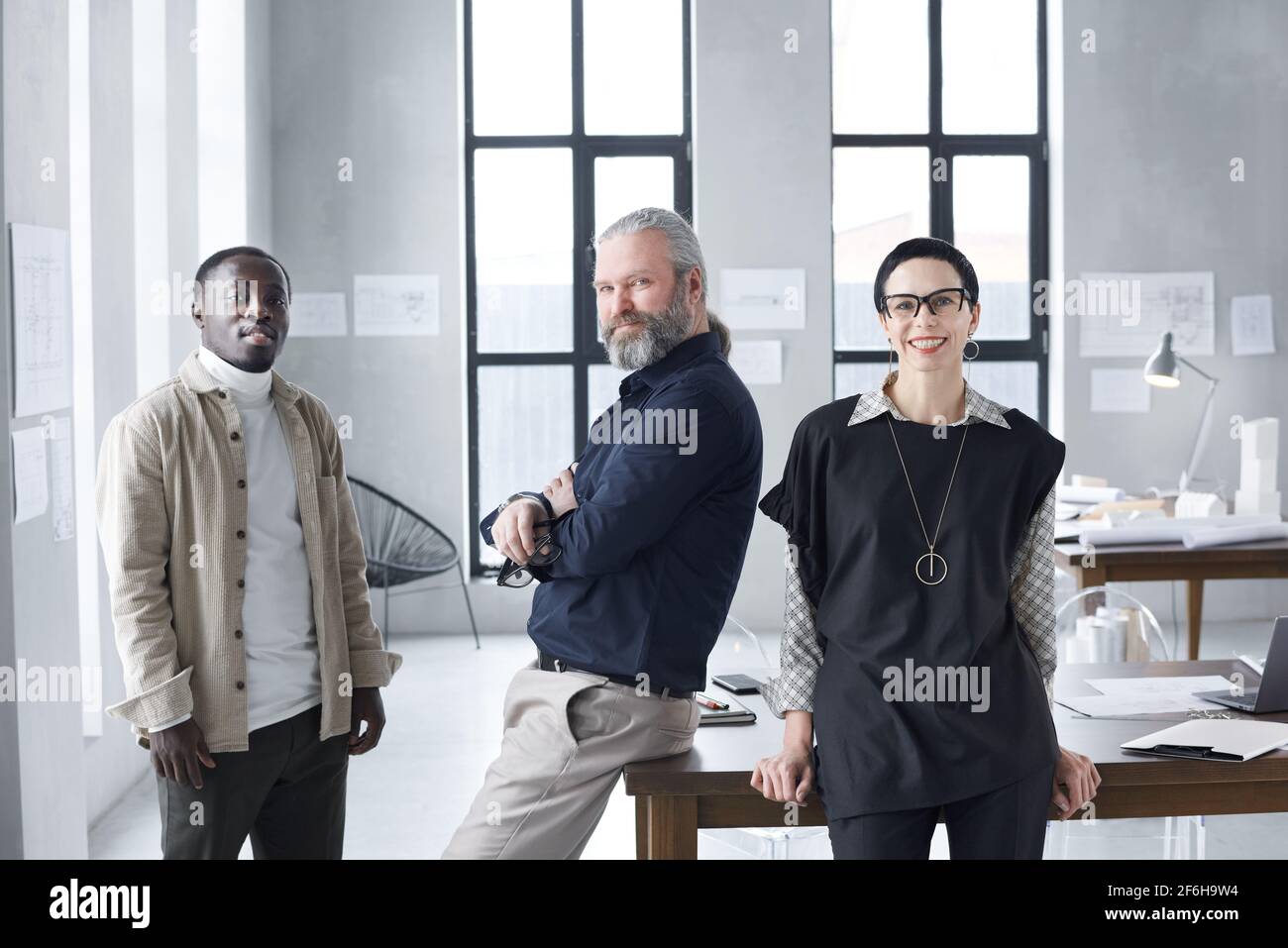Ritratto di un team di architetti che sorridono alla macchina fotografica mentre lavora insieme al modello di costruzione in ufficio Foto Stock