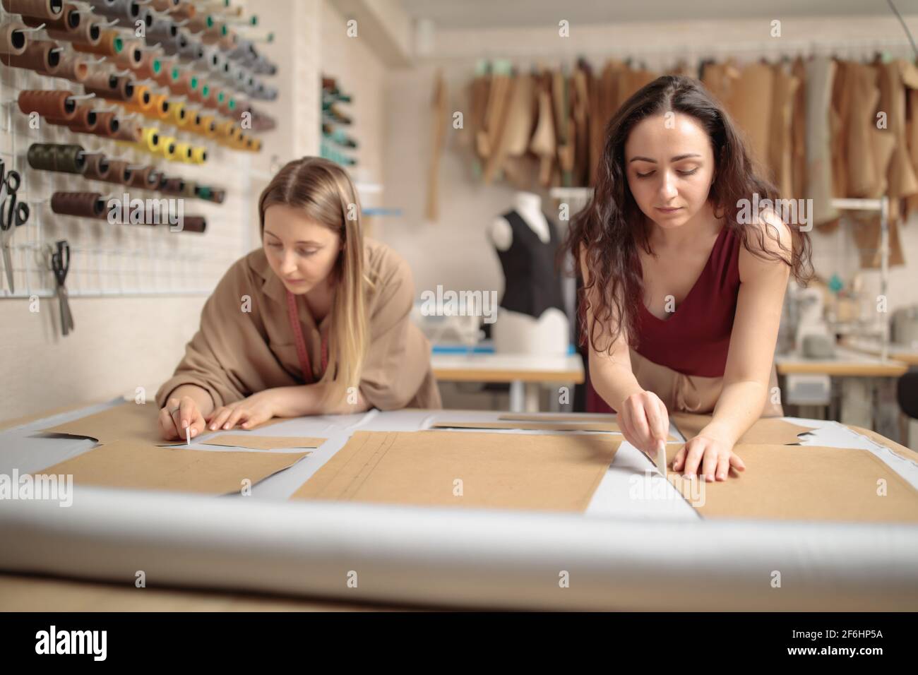 ritratto di due giovani belle donne sarti o stilisti di moda lavorare con modelli di abbigliamento in laboratorio mentre cucito classico pantaloni in Foto Stock