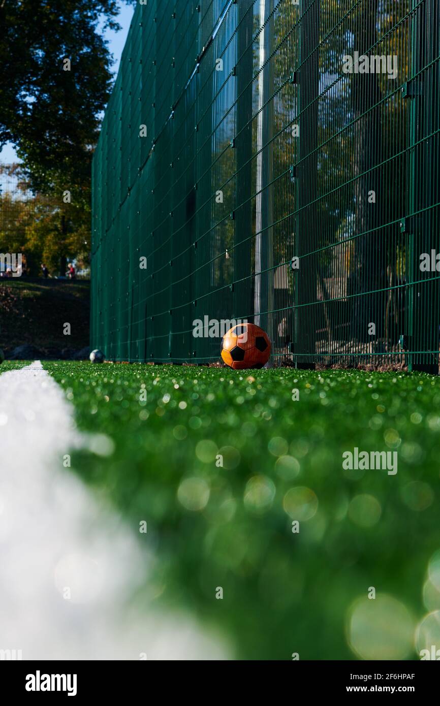 Campo di calcio vuoto artificiale con una palla arancione. Profondità di campo poco profonda. Linea bianca e spazio per la copia. Foto verticale. Giorno di sole. Foto Stock