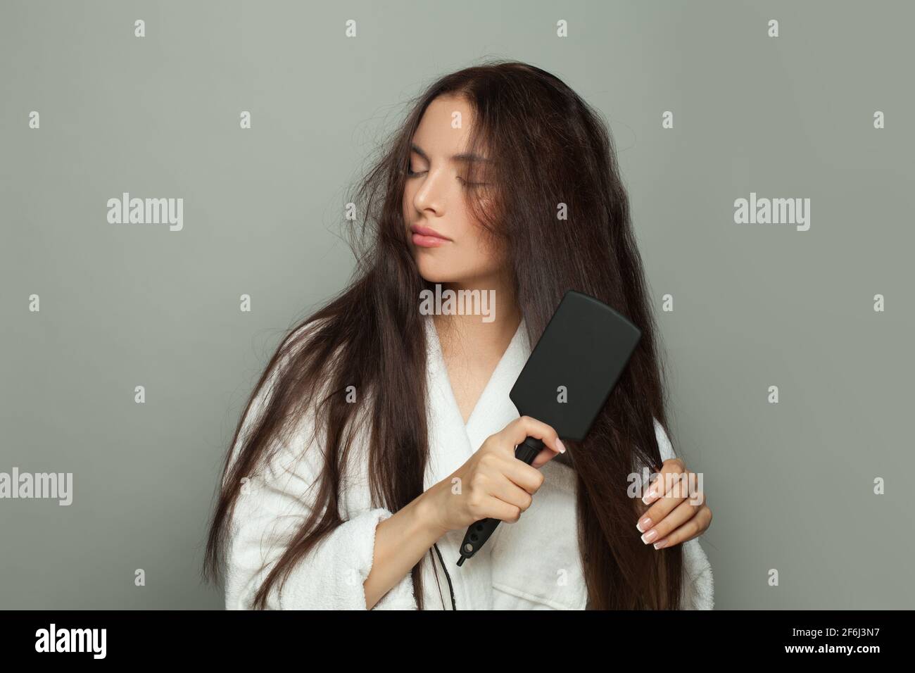 Giovane donna di brunetta che combatte i capelli aggrovigliati su sfondo bianco. Cura dei capelli e concetto di problema dei capelli Foto Stock