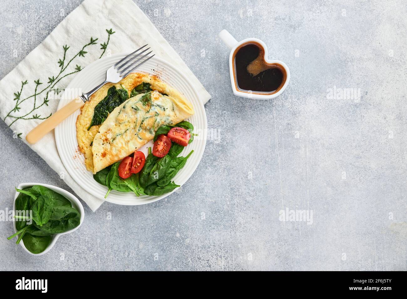 Omelette o omelette con spinaci, pomodoro di ciliegia e pepe su un piatto bianco, su fondo grigio chiaro. Concetto di colazione salutare. Vista dall'alto. Foto Stock