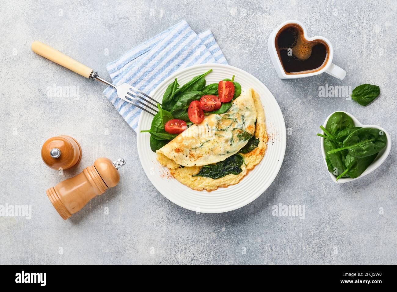 Omelette o omelette con spinaci, pomodoro di ciliegia e pepe su un piatto bianco, su fondo grigio chiaro. Concetto di colazione salutare. Vista dall'alto. Foto Stock