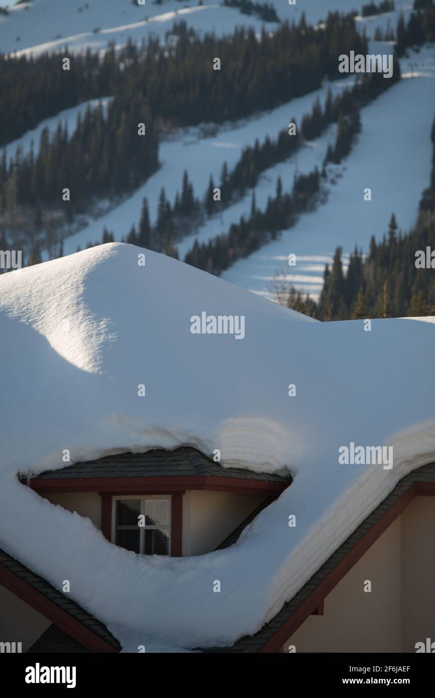 Carico pesante di neve sul tetto dello chalet di sci presso la stazione sciistica nella Columbia Britannica che mostra sci da discesa o piste da snowboard in background di alloggi di viaggio Foto Stock