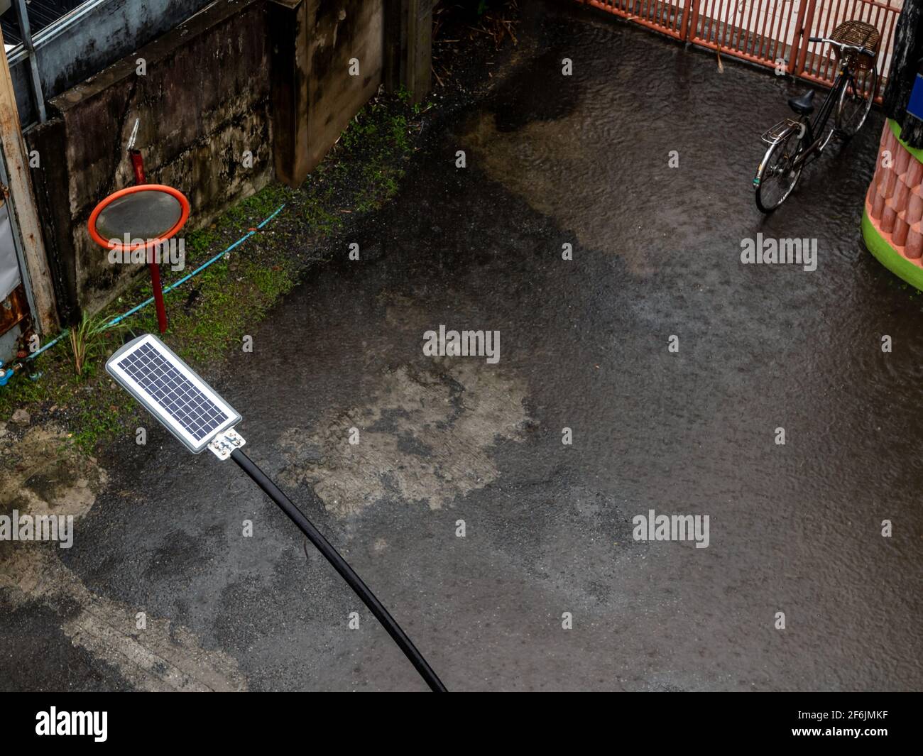 La pioggia cade su un piccolo pannello solare dietro una strada lampada in un piccolo vicolo Foto Stock