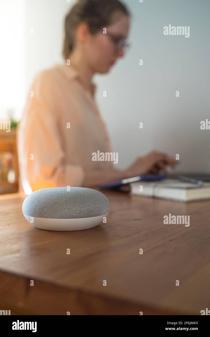 altoparlante intelligente con controllo vocale e una donna sullo sfondo in un ambiente domestico. Foto Stock