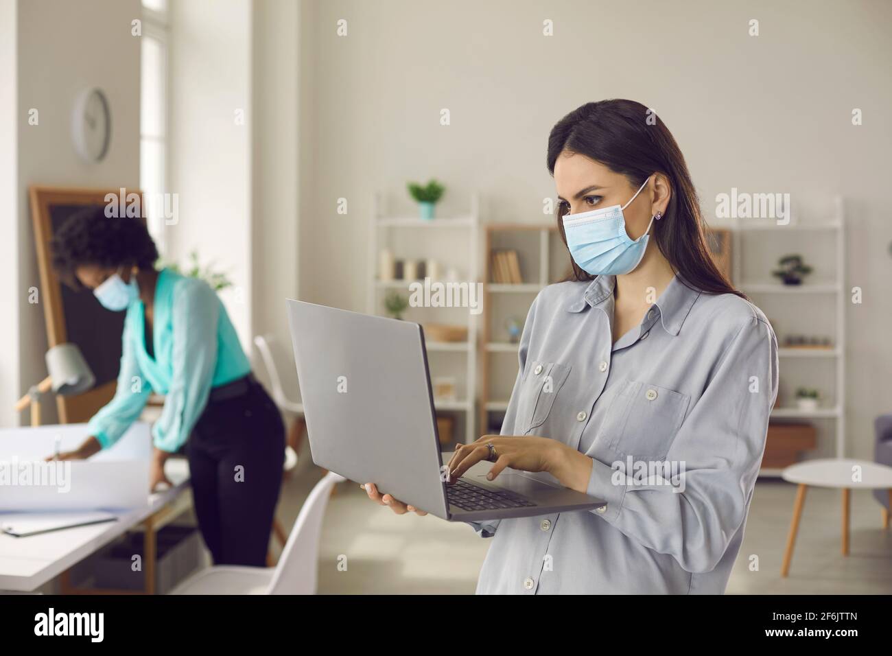 Donna dipendente che indossa la maschera facciale utilizzando il supporto per computer portatile mantenere la distanza in ufficio Foto Stock