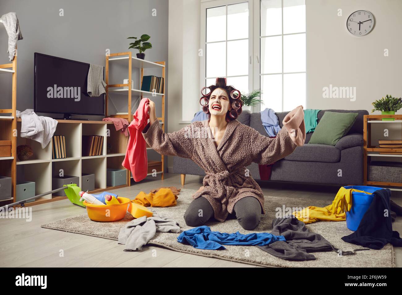 Casalinga stanca che raccoglie i vestiti dal pavimento e che si lamenta disordine costante a casa Foto Stock