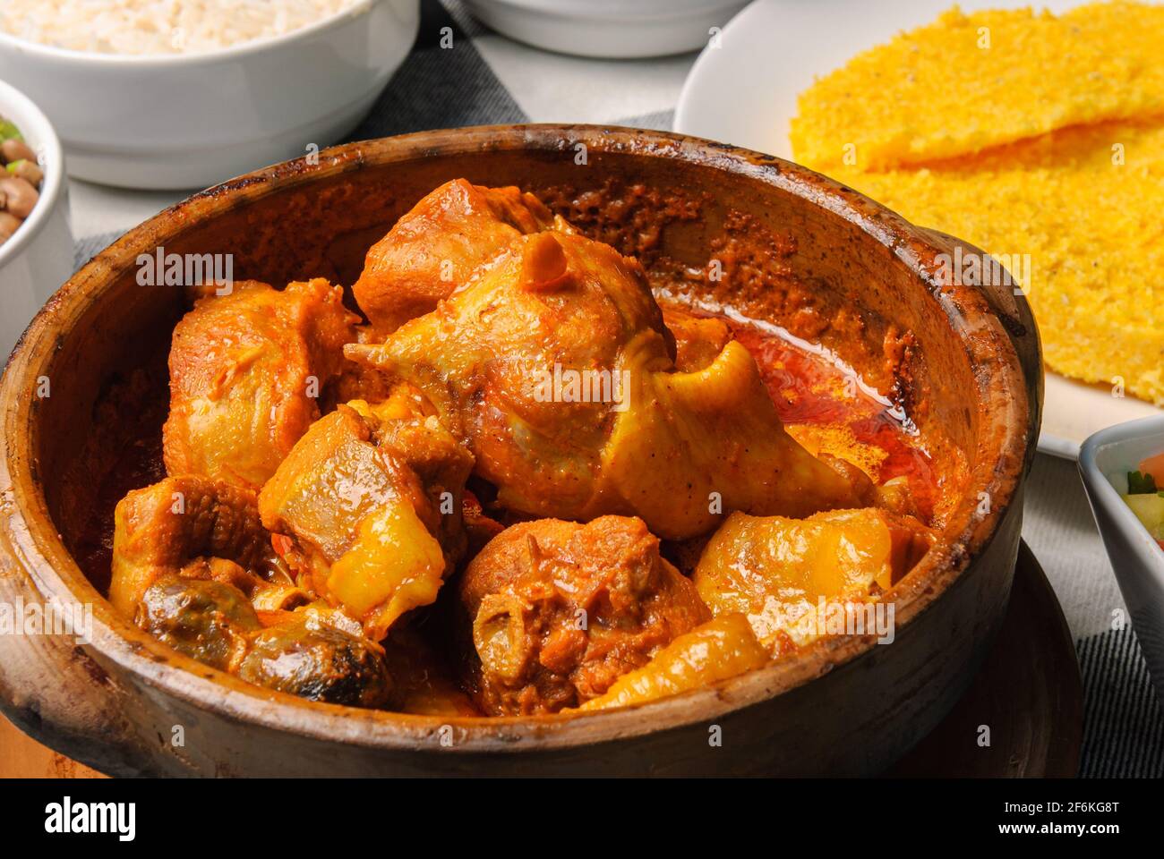 Pollo di Capoeira con couscous brasiliano, abbinato a riso, fagioli, manioca e vinaigrette, su un piatto bianco in cima a una linguetta a scacchi bianca e nera Foto Stock