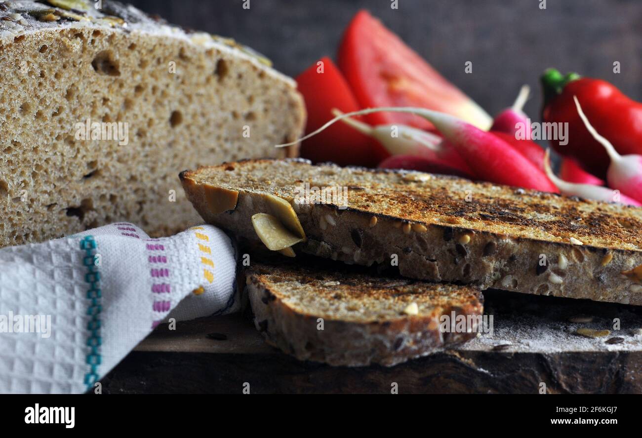 Pane affettato su un asciugamano da cucina. Verdure fresche su tavola di legno. Foto Stock