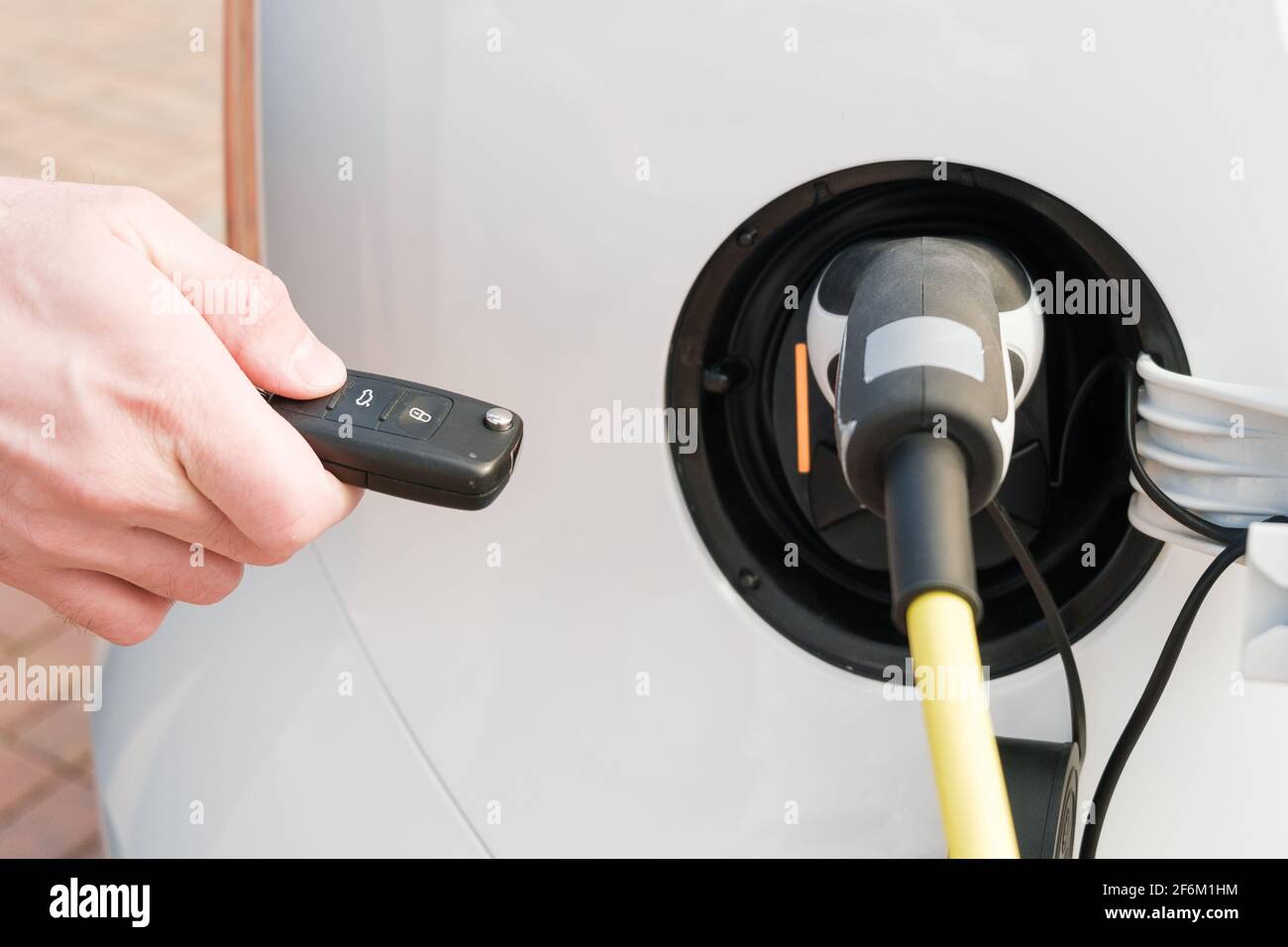 Ricarica di un veicolo elettrico con un cavo di alimentazione collegato in e mans mano sbloccandola con una chiave Foto Stock