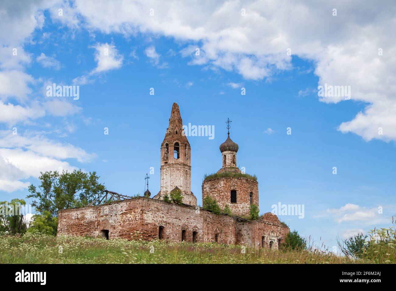 Antico cherkov distrutto contro il cielo blu. Il tempio in mattoni rossi si erge su una collina ricoperta di erba verde. Calda giornata estiva. Foto Stock