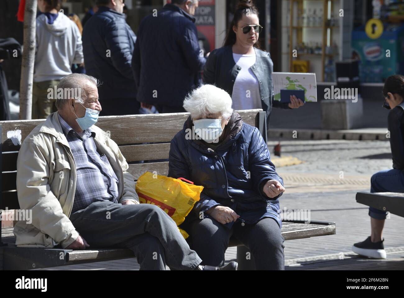 Sofia, Bulgaria - 1 aprile 2021: Due anziani seduti su una panchina in maschere protettive Foto Stock