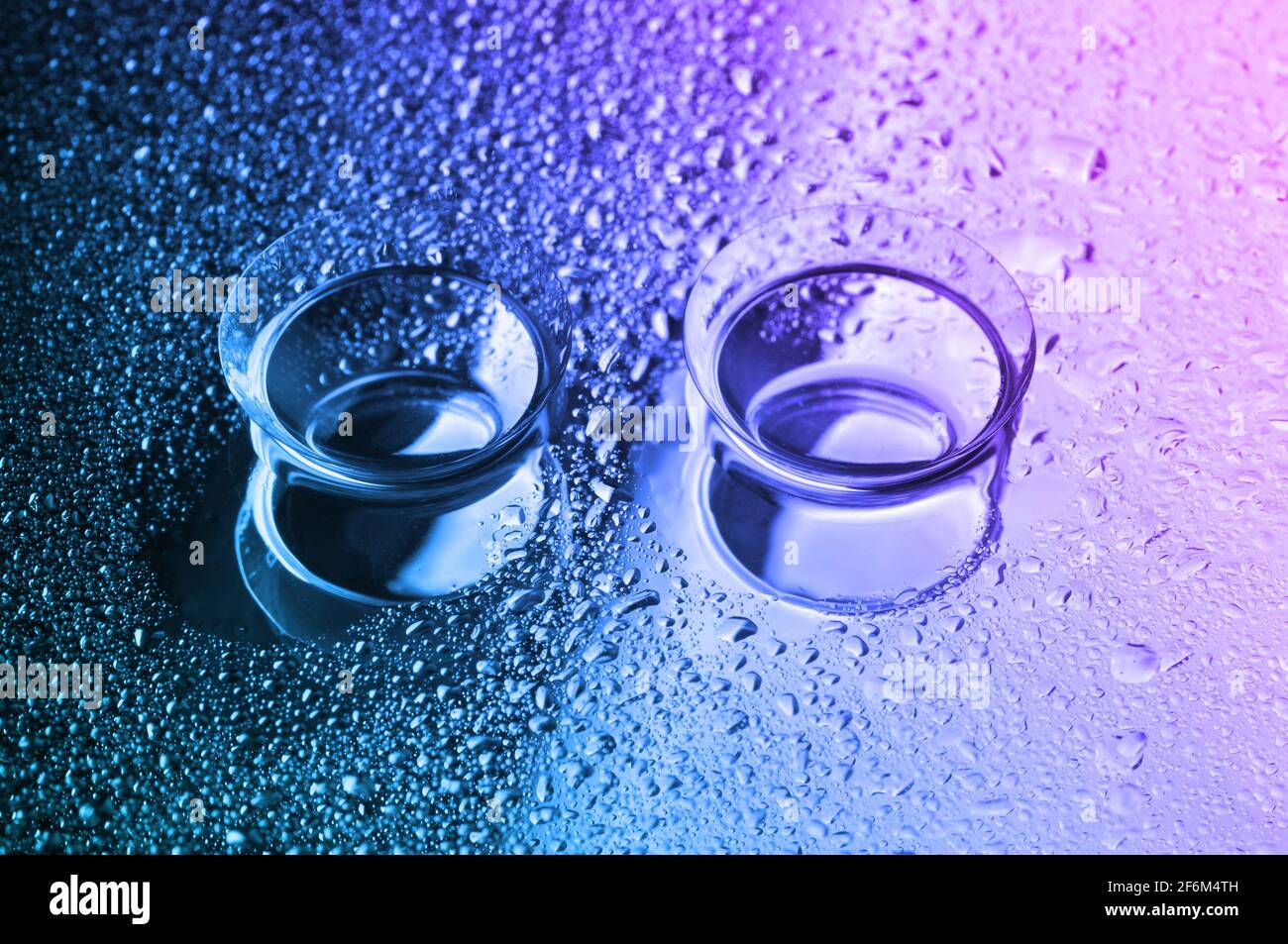 Lenti a contatto, su sfondo colorato. Due lenti a contatto con gocce d'acqua su sfondo rosa-blu-verde. Foto Stock