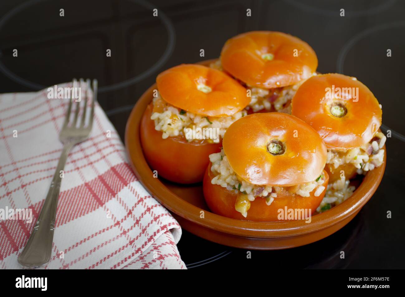 Primo piano di alcuni pomodori ripieni di riso prima di passare attraverso il forno per finire la cottura, insieme con un asciugamano da cucina e una forchetta Foto Stock