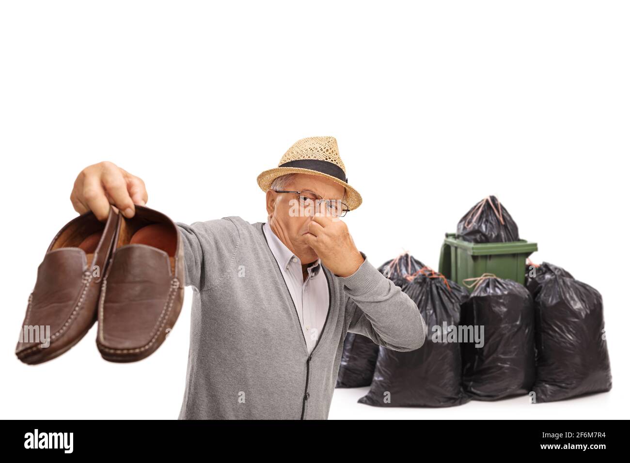 Uomo anziano che tiene un paio di scarpe stinky vicino a. contenitore e sacchetti per rifiuti isolati su sfondo bianco Foto Stock