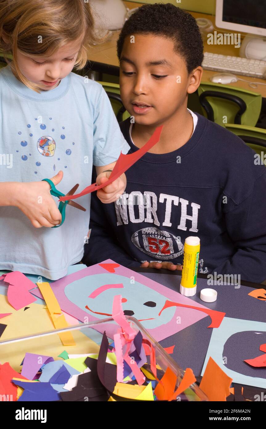 Scuola elementare indipendente di grado 4 e Kindergarten amici che usano forbici per tagliare la carta per collage come studentessa più anziana la sostiene attività artistica Foto Stock