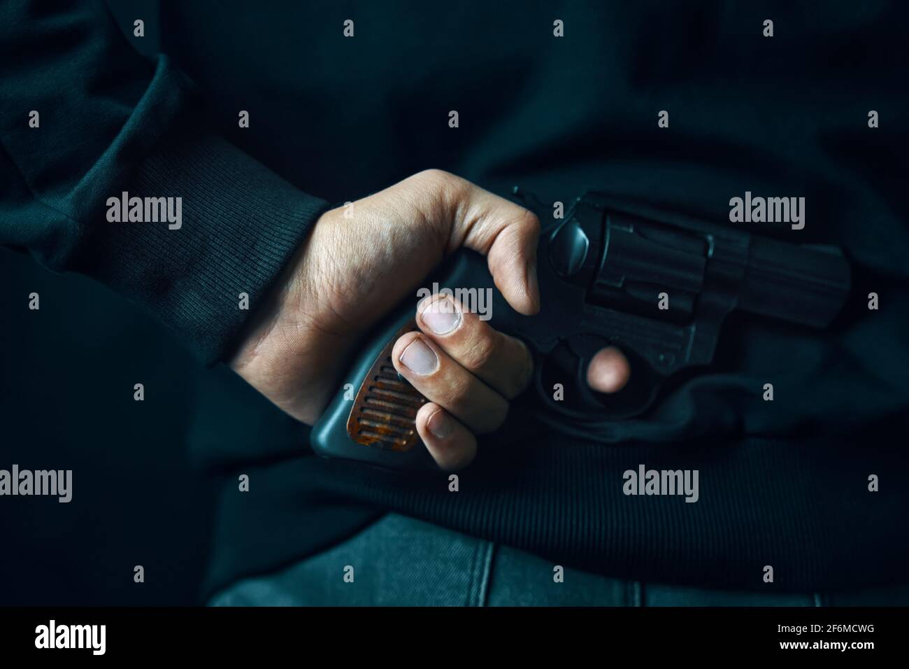 Criminale con rivoltatore sulle spalle. L'uomo in abiti scuri sta tenendo la pistola. Arma da fuoco per difesa o attacco. Assassino. Foto Stock