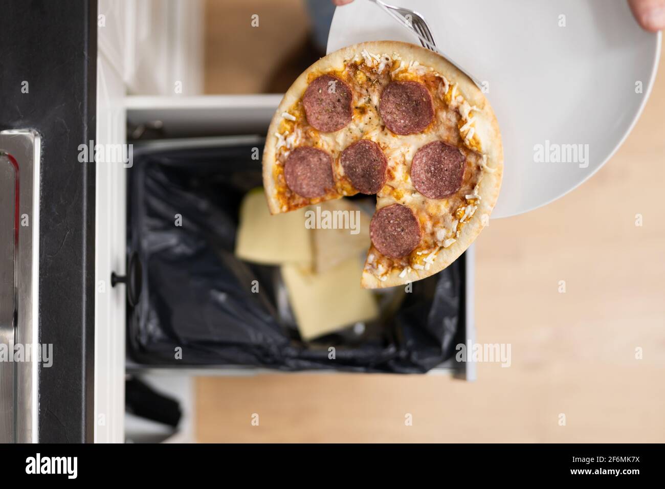 Rifiuti alimentari. Gettare via la pizza nel bidone della polvere Foto Stock